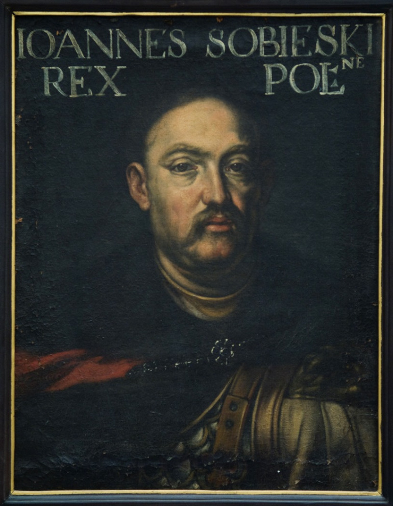 Portret Jana III Sobieskiego. Na górze obrazu napis: IOANNES SOBIESKI REX POL. Obraz przedstawia realistyczny portret Jana III Sobieskiego. Król ubrany w zbroję, z płaszczem na ramionach. Wizerunek namalowany jest realistycznie z dbałością o każdy szczegół.