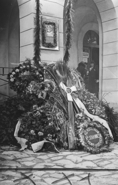 Czarno-białe zdjęcie archiwalne. Dokumentuje tablicę pamiątkową ku czci Jana Sobieskiego. Fotografia pochodzi z lat 1918-39. Przedstawia wieńce złożone pod tablicą ku czci Jana Sobieskiego, która znajduje się na budynku ratusza w Samborze.
