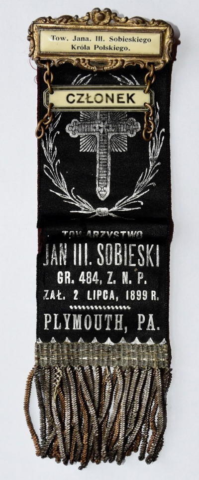 Szarfa Towarzystwa im. Jana III Sobieskiego. Na czarnym materiale w kształcie wstążki zakończonej na dole frędzlami, u samej góry przypięty emblemat "członek" i poniżej napis Jan III Sobieski.